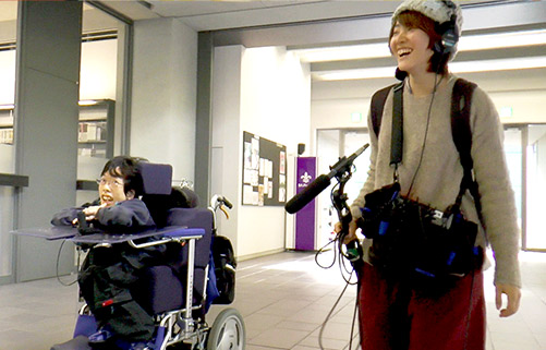 車椅子の石田監督と録音マイクを持つ録音の本田さんが歩いている様子